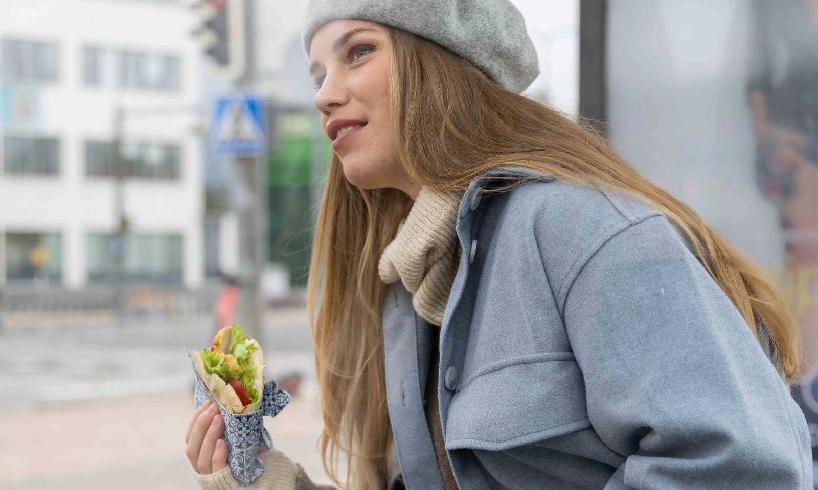 A young woman in traffic, eating her lunch - We offer versatile food solutions for all situations